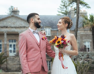 Une mariée et un marié se tiennent devant un manoir élégant, vêtu de leurs habits de mariage