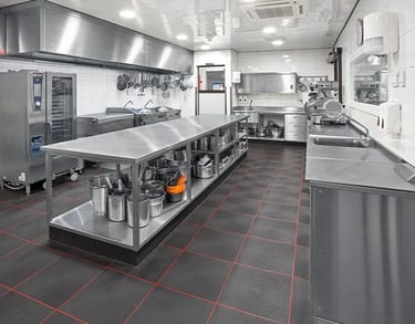 Large professional kitchen layout showing prep areas and stainless steel benches with sink along the wall.