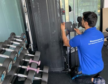 Professional technician performing gym equipment maintenance on a cable machine next to a dumbbell rack.