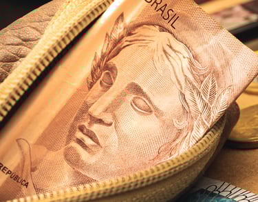 imagem de uma bolsa pequena com dinheiro dentro e moedas ao fundo  de uma mesa 