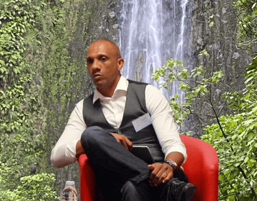 Bruno Valery lors d’une conférence sur le tourisme en Guadeloupe, avec les chutes du Carbet en arrière-plan.