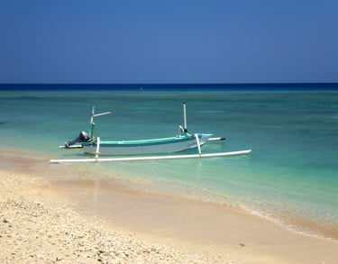 A traditional Indonesian outrigger boat moored on a tropical beach with turquoise water in Bali