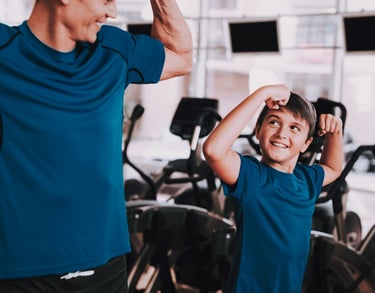 Un adulto e un bambino in palestra che mostrano i muscoli in modo giocoso, creando un momento divertente e motivante durante