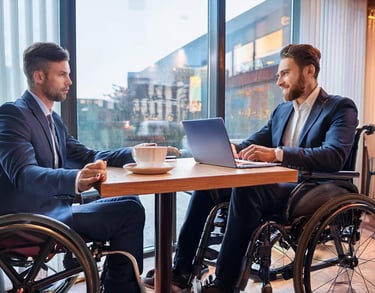 Zwei Rollstuhlfahrer sitzen für ein Beratungsgespräch in einem Café