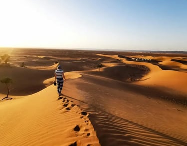 Woman in striped top walking along the crest of a Sahara Desert sand dune
