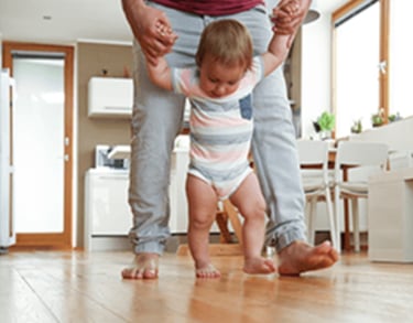 a man holding a baby's hand while standing on a hardwood floor