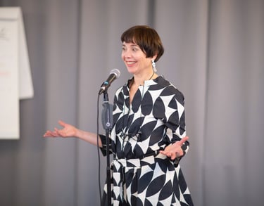 Female public speaking trainer behind microphone, energetic smiling while teaching.