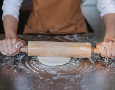Panadero estirando masa sobre una superficie metálica enharinada con un rodillo de madera
