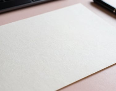 A close-up of a high-quality textured paper with subtle Japanese calligraphy, placed on a light pink desk surface.