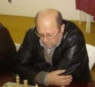 A focused male chess player wearing glasses and a leather jacket during a competitive chess tournament match.