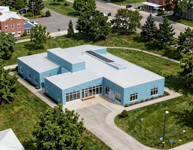 An aerial view of a vibrant, clean community center in a North American town, surrounded by green spaces and featuring modern architectural lines in light blue.