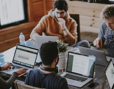 a group of people sitting around a table with laptops