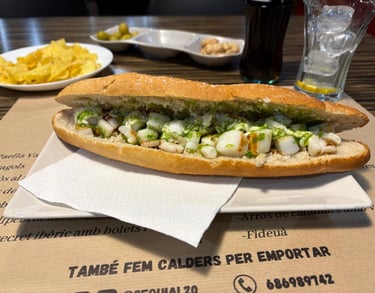 Grilled cuttlefish sandwich with green parsley garlic oil served on a baguette with chips and olives.