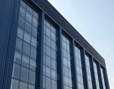 A photography shot of the exterior of a sleek, modern industrial building in a Pakistani business district, characterized by large glass windows and steel blue architectural panels. The sky is clear and bright.