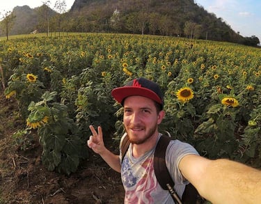 Smiling taking a selfie in a blooming sunflower field with mountains in the background.