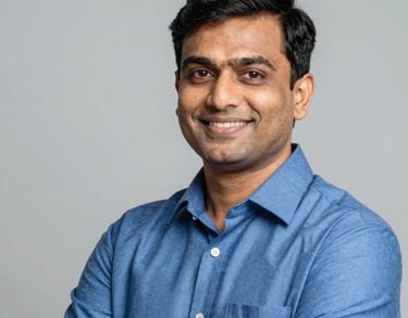 A professional portrait of a South Asian male educator in a smart blue shirt, smiling with a sense of purpose against a clean, premium background.