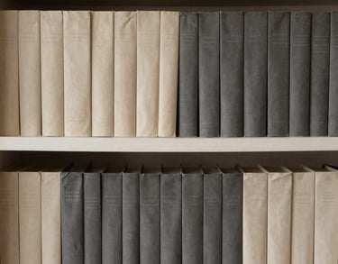 A close-up of a shelf filled with books, organized by color in shades of cream and charcoal grey. Minimalist home library in a South American residence.