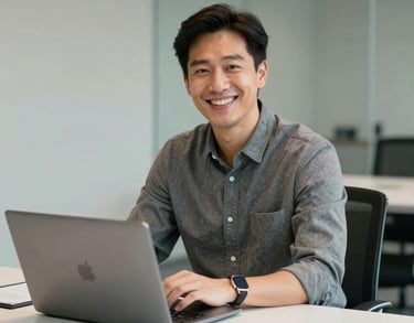 Portrait of a smiling professional in business casual attire sitting at a clean, white conference table with a laptop. Professional setting, North American / US.