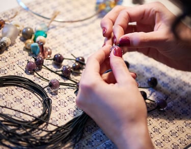 Manos creando una pulsera de macramé con cuentas y cordones artesanales.