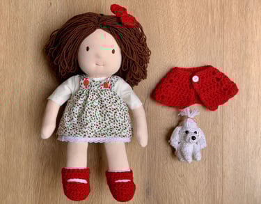 Muñeca Waldorf hecha a mano con cabello castaño, vestido floral, zapatos rojos y un pequeño perrito 