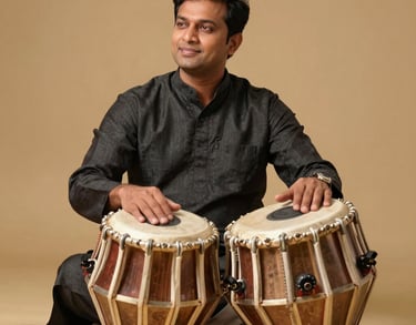 Professional portrait of a male South Asian / Indian percussionist in a charcoal black kurta, sitting gracefully with a pair of professional tablas, warm gold lighting, premium photography.