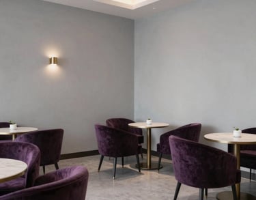 A sophisticated tea lounge in a North American spiritual center with dark purple velvet chairs, light gray walls, and elegant minimalist decor.