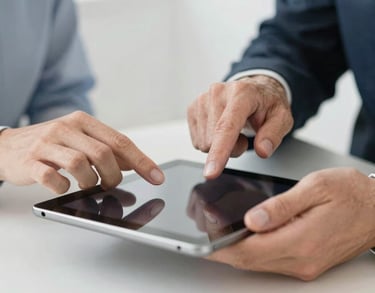 Close-up of two pairs of hands—one younger, one older—working together over a tablet in a modern office, representing technology access and mentorship, soft pearl white background.