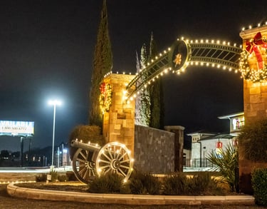 Stone archway with Christmas lights and a decorative cannon at a commercial shopping center at night.