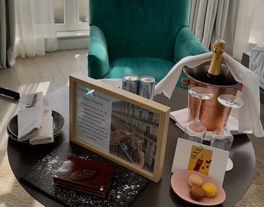 a table with a bottle of champagne, card, cake, macaroons, dessert, and framed letter