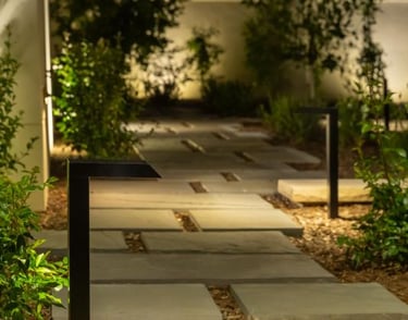 Modern black LED path lights illuminating a stone paver walkway in a landscaped garden at night.