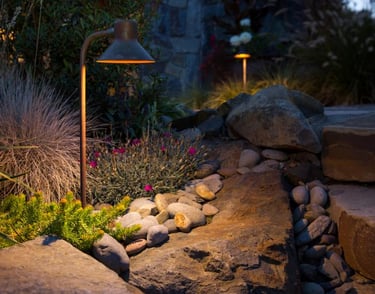 Low voltage landscape path lights illuminating a garden rockery and stone steps at dusk.