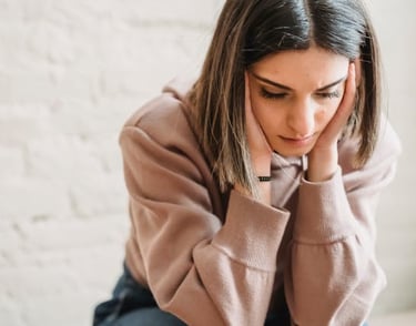 Stressed young woman in a pink hoodie holding her head in her hands, reflecting anxiety and mental fatigue.