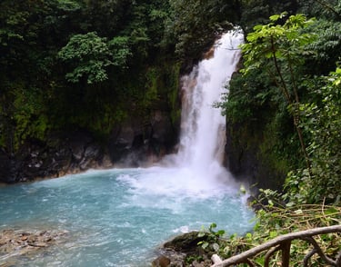 A powerful tropical waterfall cascading into a bright turquoise pool surrounded by lush green jungle foliage.