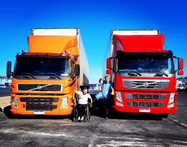 dois grandes caminhões com dois caminhoneiros junto aos caminhões onde um é cadeirante