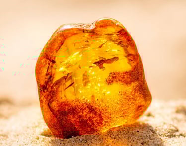 Una pieza cruda de resina de ámbar translúcida dorada natural que descansa en arena
