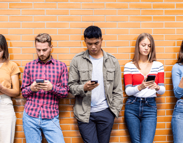 Teenagers leaning against a wall, fiddling with their smartphones.