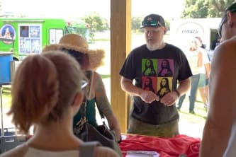 a man in a hat is volunteering at a booth and a woman in a hat is visiting the booth