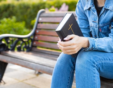 Girl sitting on a park bench holding a bible 