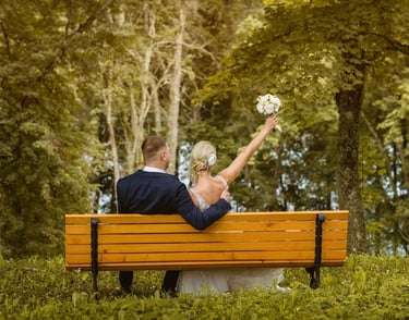 a bride and groom sitting on a bench in a park