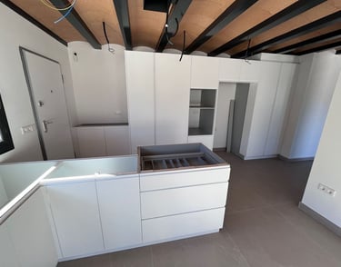 Cuisine moderne blanche avec placards sans poignées, îlot central et plafonds industriels voûtés