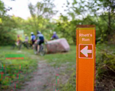 Group of bikers in the background of a focus shot on the "Rhett's Run" signange