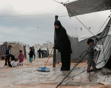 femme réfugiés gaza devant sa tente en train de nettoyer le sol, ses enfants jouent à l'extérieur dans la boue