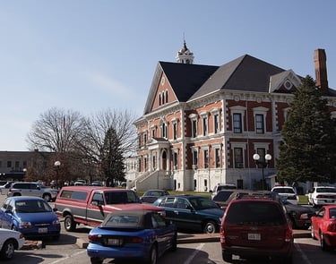 Historic brick courthouse with a white clock tower and parking lot full of cars Macomb IL