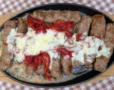 Sizzling platter of Balkan cevapi sausages topped with melted cheese and red peppers.