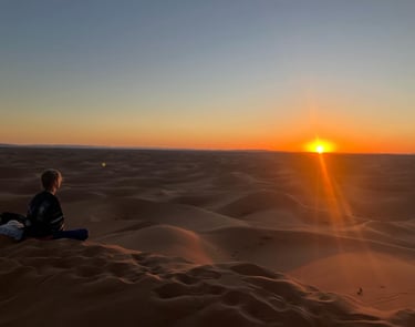 Traveller sitting cross‑legged on Erg Chigaga dune at sunset