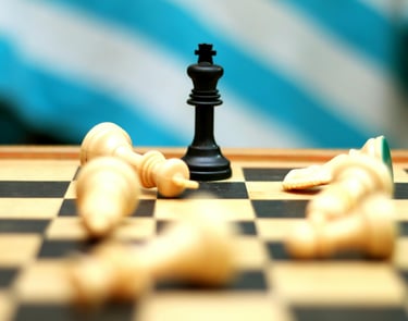 Black king chess piece standing victorious among fallen white pieces on a wooden game board.