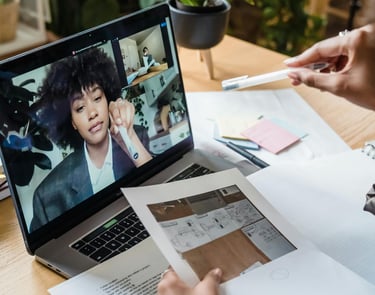 Professional architect reviewing floor plans during a remote video conference on a laptop.
