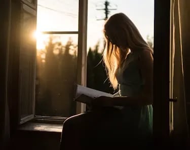 woman reading book for bible answers while sitting at window