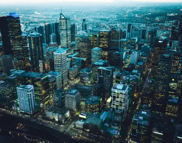 Aerial night view of illuminated Melbourne city skyline with glowing office skyscrapers and street lights.