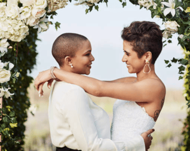 a lesbian couple at their wedding celebration under the arbour / bower dress in white 
